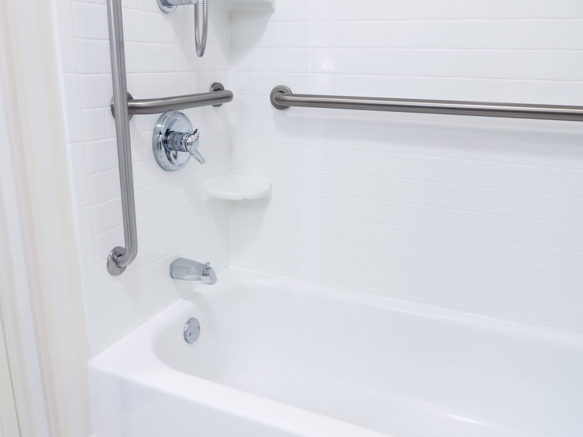 White bathtub with chrome fixtures, grab bars, and a showerhead in a tiled bathroom.