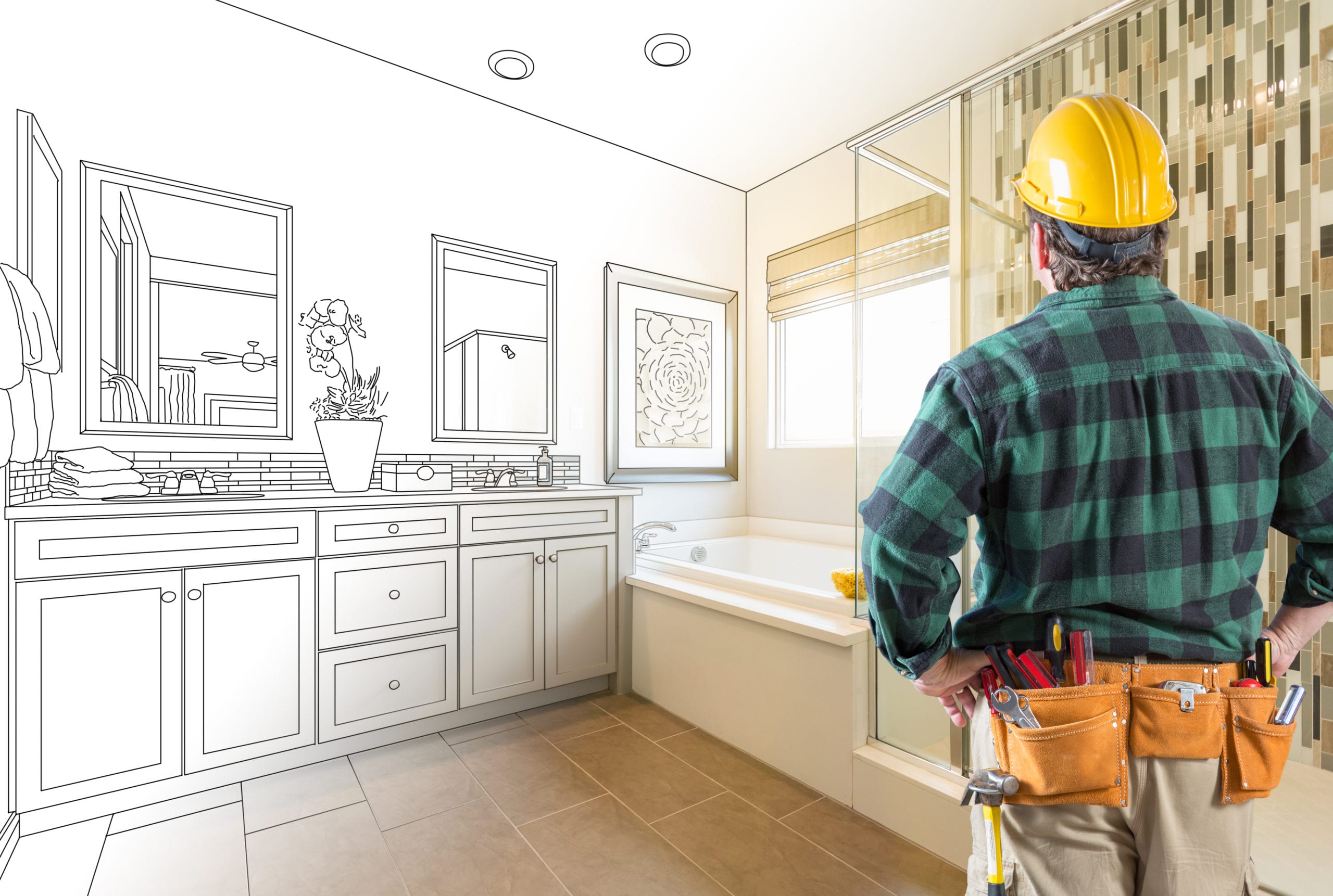 Construction worker in a hard hat and tool belt stands in a bathroom, looking at a partially sketched and partially finished room.