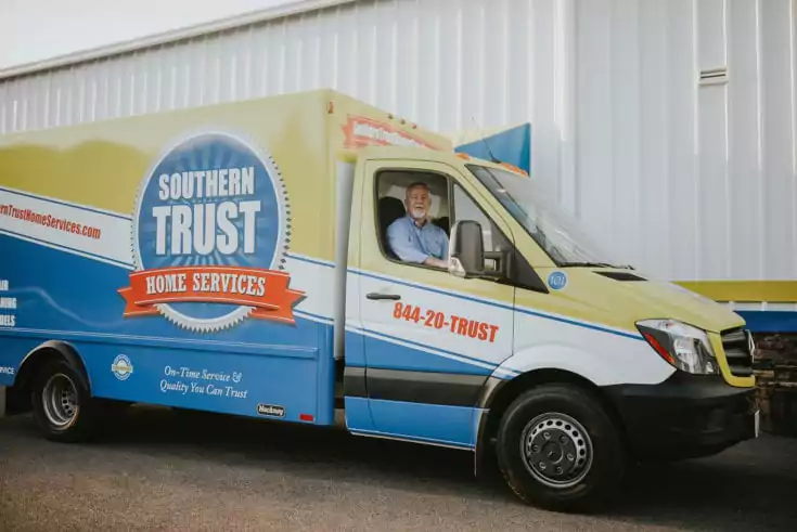 A Man Sits In A Southern Trust Home Services Van, Parked By A White Building. The Vehicle Proudly Displays The Company Logo Along With A Contact Number For Quick And Reliable Service.