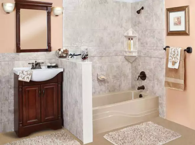 A Bathroom With A Wooden Vanity And Mirror, A Beige Bathtub, Wall Tiles, And Brown Fixtures. Towels Hang On A Rack, And A Framed Picture Is On The Wall. Two Textured Rugs Are On The Floor.