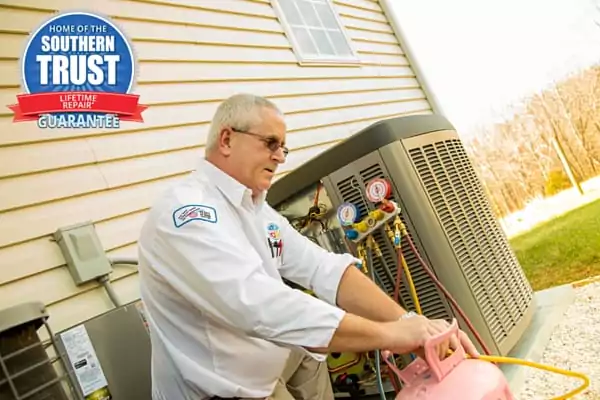 A Technician In A White Shirt Works On An Outdoor Hvac Unit With Tools And A Refrigerant Tank Nearby. A Logo Reading &Quot;Southern Trust Lifetime Repair Guarantee&Quot; Is In The Top Corner.
