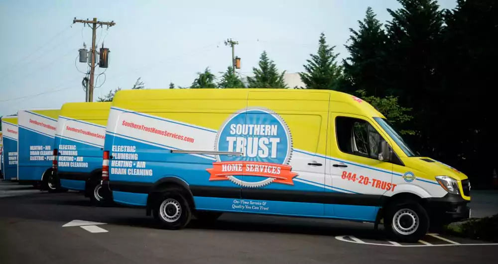 Three Southern Trust Home Services Vans Are Parked In A Row, Displaying Branding And Services Like Electrical And Plumbing On Their Sides.