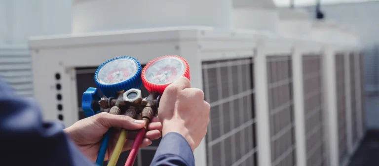 On a rooftop, a person is engaged in air conditioning maintenance, using a manifold gauge set to measure the pressure of an HVAC system.