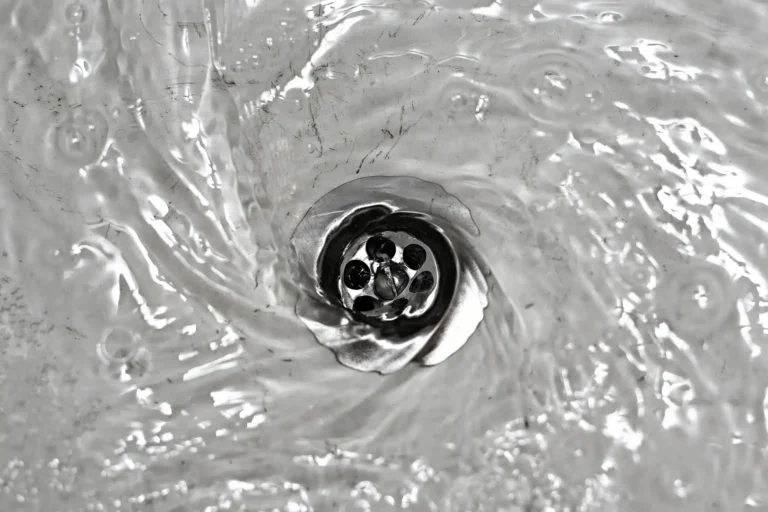 Water swirling down a metal sink drain forms a captivating circular vortex, reminiscent of the seamless efficiency provided by professional drain clearing services.