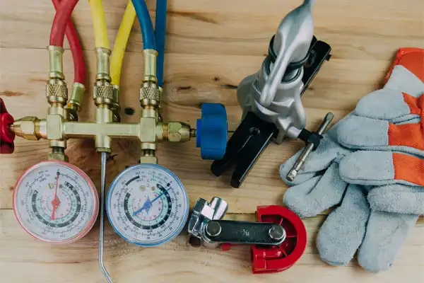 HVAC tools for general heating installation are displayed on a wooden surface, featuring a gauge manifold, pipe cutter, gloves, and other essential maintenance equipment.