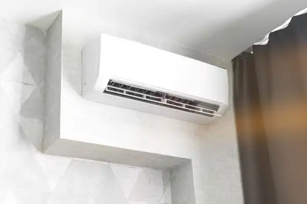A wall-mounted air conditioner, ideal for mini split repair, is positioned above a window with gray curtains, installed on a light-colored wall.