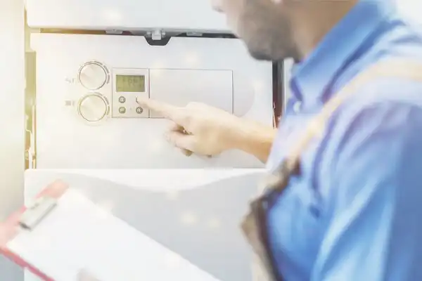 A person in a blue uniform expertly adjusts controls on machinery, clipboard in hand, ensuring the seamless operation of a tankless water heater installation.