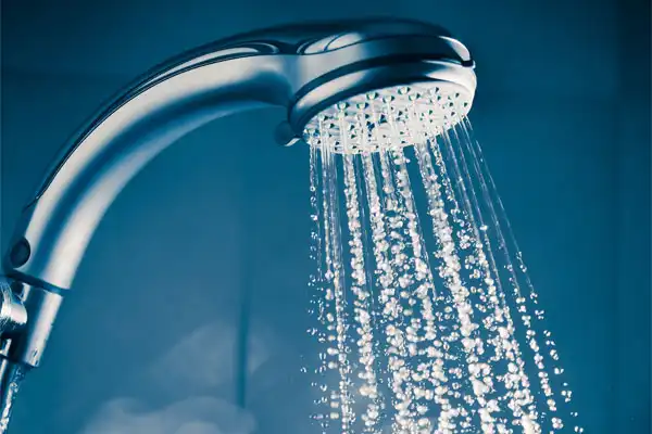 Close-up of a showerhead spraying water with droplets in motion against a blue background, showcasing the seamless flow one might experience after a tankless water heater repair.