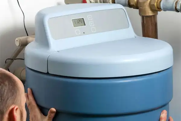 A person is expertly adjusting a blue water softener with a digital control panel, mastering the art of water softener installation.