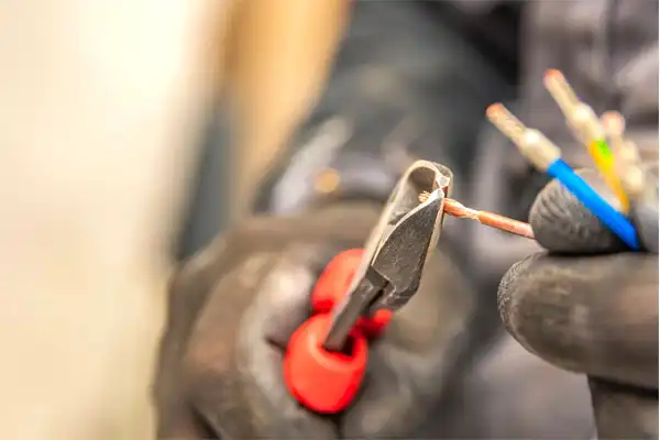 Close-up of a person engaged in general electrical installation, using red-handled wire cutters to strip insulation from wires, all while wearing protective gloves.