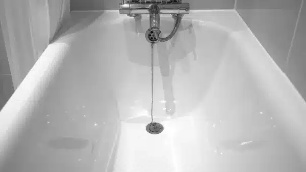 A White Bathtub With A Faucet And A Metal Drain Plug Chain Hanging Down, Set Against Tiled Walls.