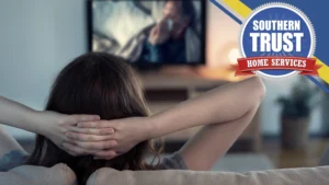 A Person Sits On A Couch With Hands Behind Their Head, Watching Tv; A Southern Trust Home Services Logo Appears In The Top Right Corner.